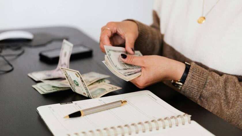 Close-up of person counting cash with notepad on desk, indicating financial tasks.