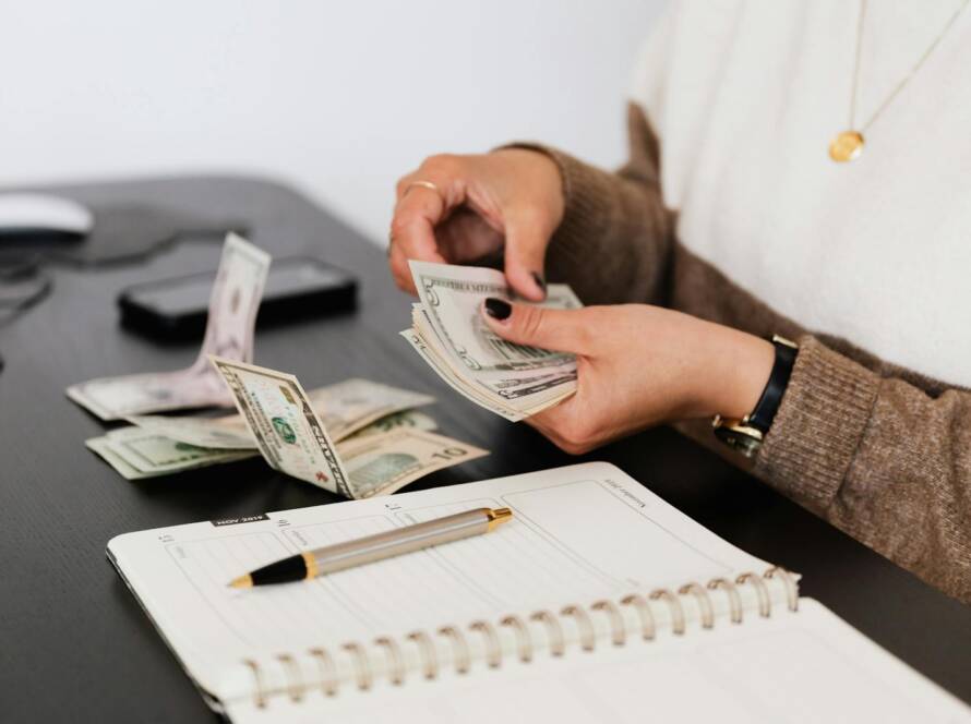 Close-up of person counting cash with notepad on desk, indicating financial tasks.